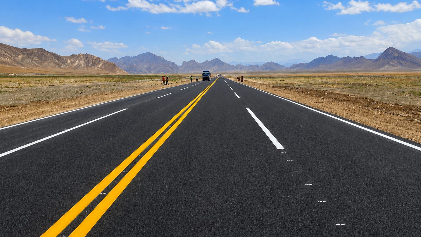 Completed asphalt highway with double yellow centre line running toward mountains on the Aynak copper mine access road in Logar province